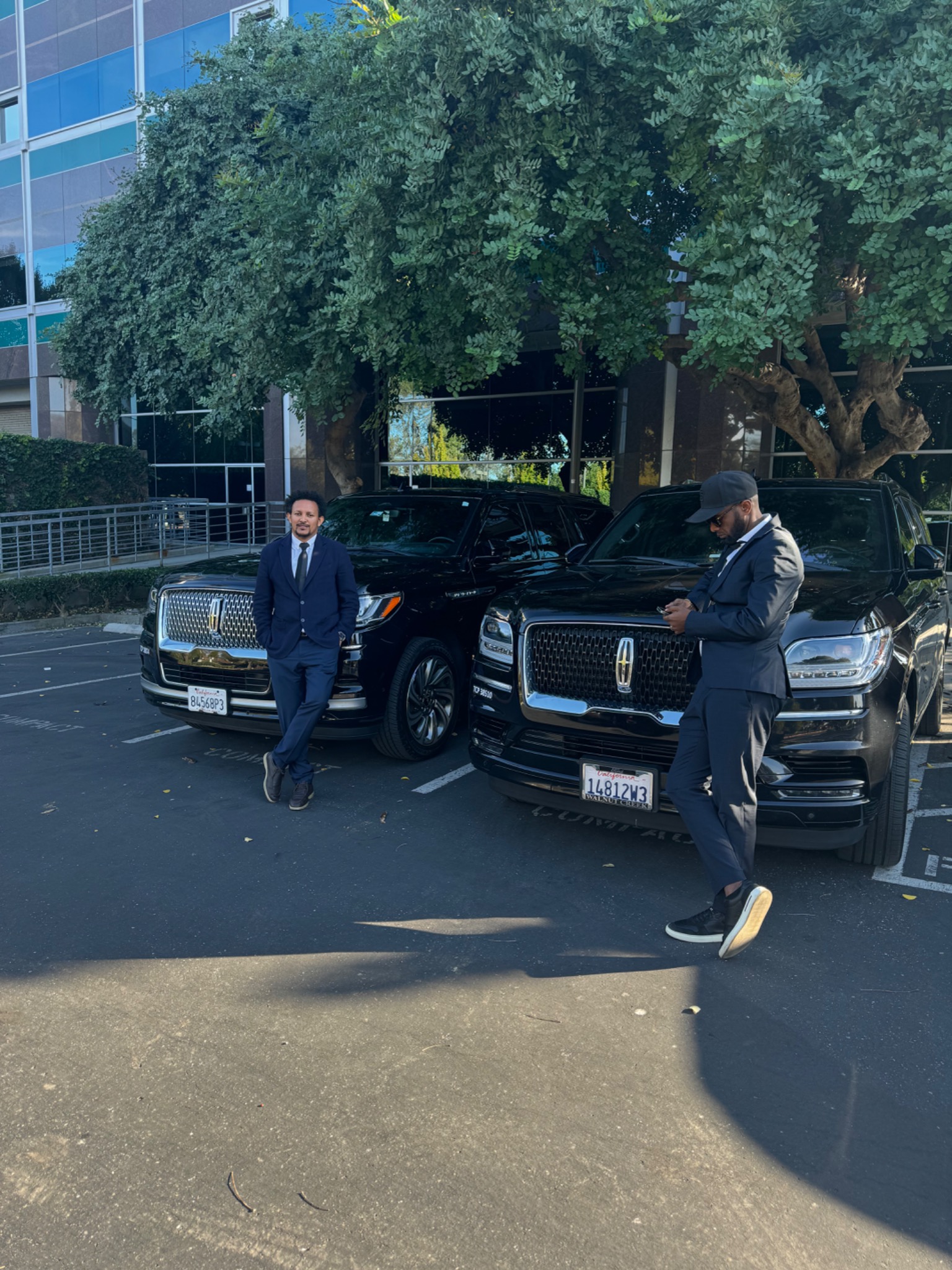 Two professional chauffeurs standing beside black luxury SUVs